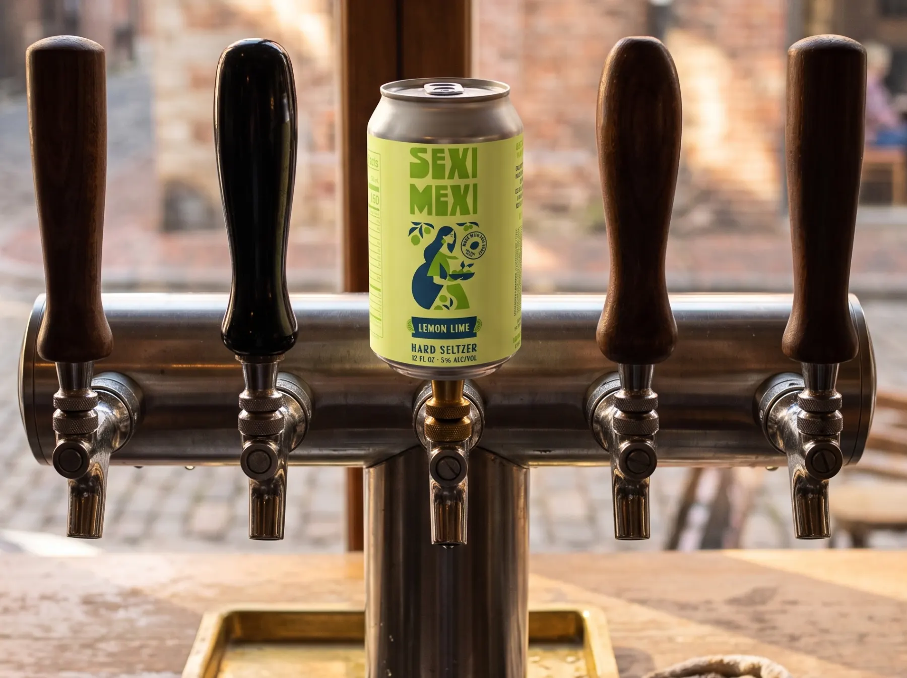 A SEXI MEXI Lemon Lime tap handle, shaped like the can, in the middle of a row of plain handles on a taproom draft tower